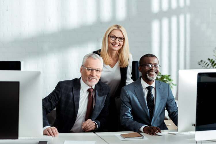 cheerful blonde woman smiling while standing near happy multicultural partners